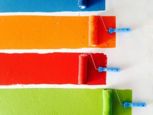 Four paint rollers each rolling bright colors of paint across a white background.